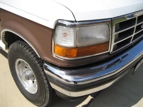 White and brown Ford Bronco front corner with chrome bumper and grille. Visible tire and headlight