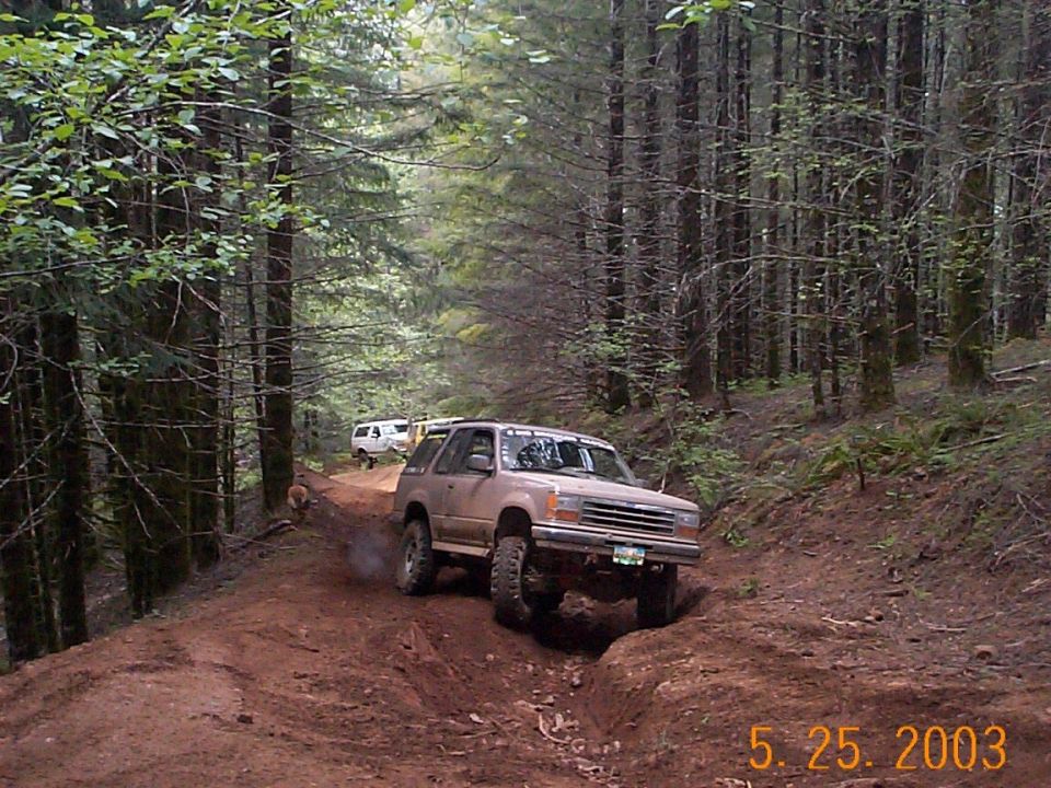 Tan lifted SUV on big tires navigating a muddy forest trail