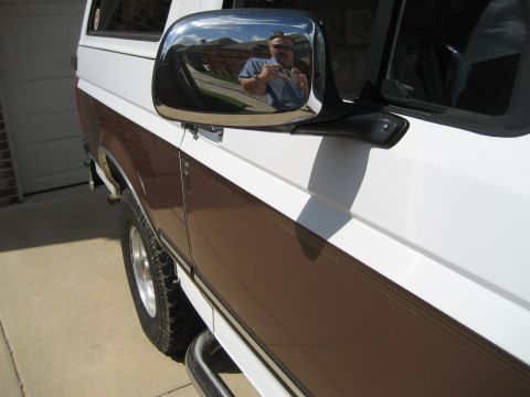 White and brown Ford Bronco side view, showing chrome side mirror reflecting a man taking the photo