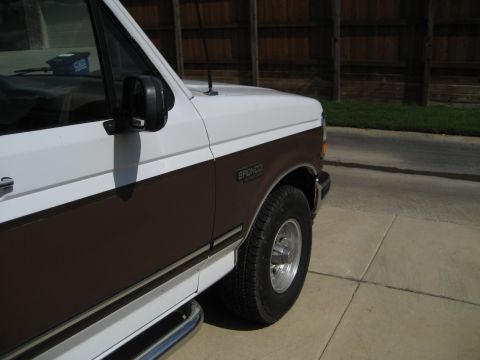 1993 Ford Bronco - The side profile of a white and brown 1993 Ford Bronco shows its distinctive two-tone paint scheme and fender badging.