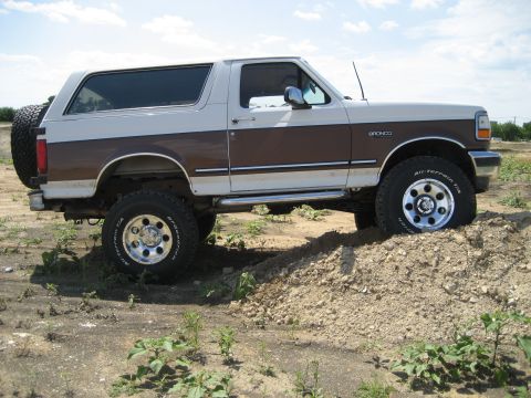 1993 Ford Bronco - This lifted Ford Bronco is shown off-road, navigating a dirt incline with its distinctive two-tone paint scheme.