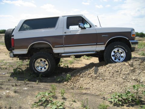 1993 Ford Bronco - This lifted 1993 Ford Bronco is shown in a side profile, navigating a dirt mound with its off-road tires.