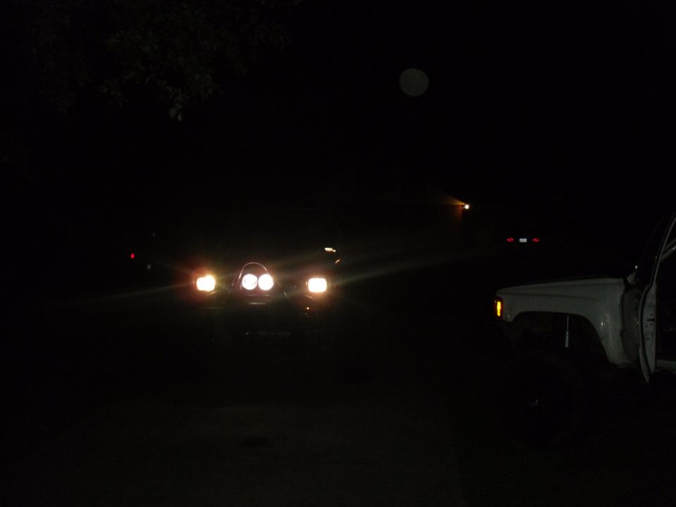 Front view of a dark SUV with headlights on, and a white SUV to the right with its door open