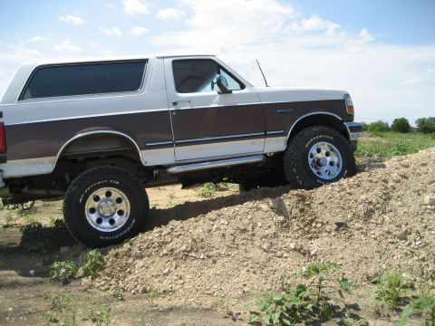 1993 Ford Bronco - This lifted 1993 Ford Bronco is shown in a three-quarter front view, navigating a dirt incline.