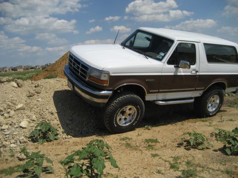 1993 Ford Bronco - This Ford Bronco is parked on a dirt lot with a hill and some houses in the background.