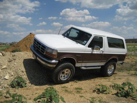 1993 Ford Bronco - A two-tone Ford Bronco sits on a construction site under a partly cloudy sky.
