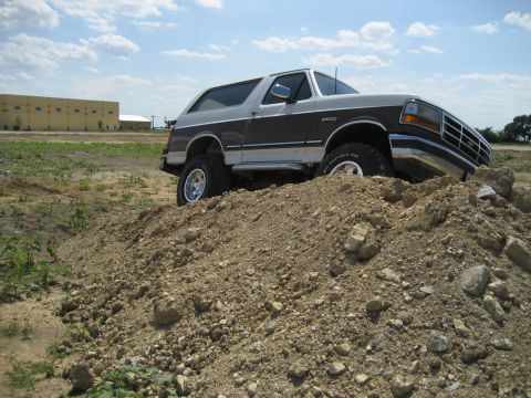 1993 Ford Bronco - This lifted Ford Bronco navigates a dirt pile under a partly cloudy sky.