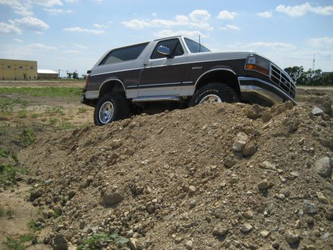 1993 Ford Bronco - A two-tone 1993 Ford Bronco navigates a dirt pile under a partly cloudy sky.