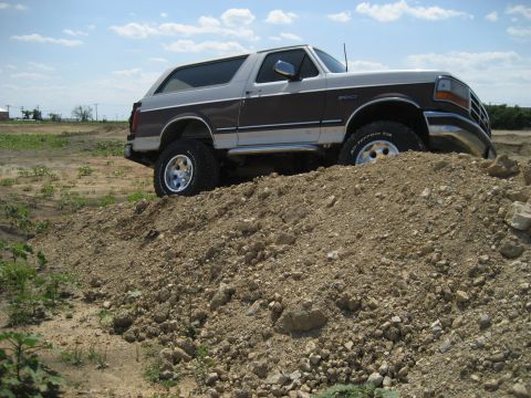1993 Ford Bronco - Ford Bronco navigating an off-road obstacle on a sunny day.