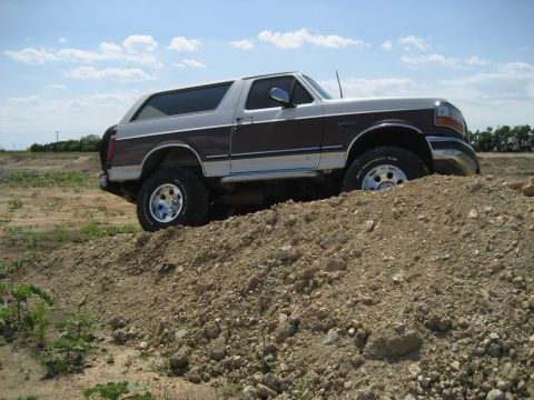 1993 Ford Bronco - A two-tone Ford Bronco is shown navigating a dirt hill on a sunny day.