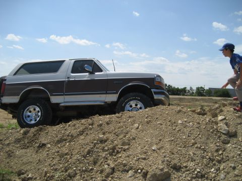 1993 Ford Bronco - A two-tone Ford Bronco navigates a dirt obstacle under a partly cloudy sky.