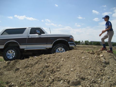 1993 Ford Bronco - A Ford Bronco is partially stuck in a dirt mound with a young person standing on top of the mound.