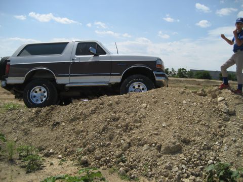1993 Ford Bronco - A two-tone Ford Bronco is shown navigating an off-road course with a young observer.