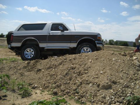 1993 Ford Bronco - A two-tone brown and white Ford Bronco is shown off-road, navigating a dirt incline with a spare tire mounted at the rear.