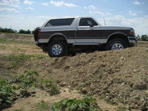 1993 Ford Bronco - This lifted 1993 Ford Bronco is shown off-road on a dirt pile under a partly cloudy sky.