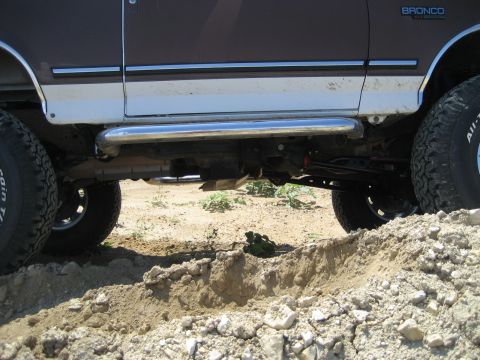 1993 Ford Bronco - A 1993 Ford Bronco with off-road tires and running boards navigates a dirt track.