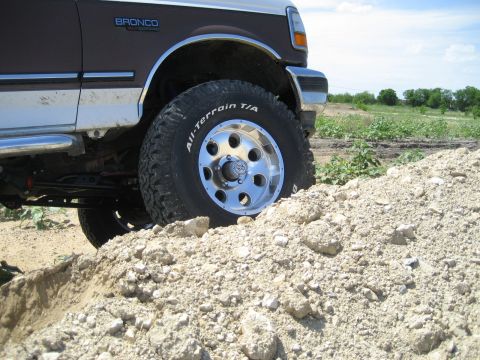 1993 Ford Bronco - This 1993 Ford Bronco is shown with its front wheel on a dirt pile, highlighting its lifted suspension and off-road tires.