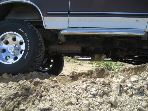 1993 Ford Bronco - Side view of a lifted 1993 Ford Bronco with off-road tires navigating rough terrain.