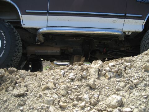 1993 Ford Bronco - The side of a lifted Ford Bronco is shown with its running boards and undercarriage, positioned on a rocky, dirt surface.