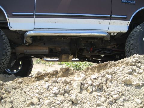 1993 Ford Bronco - A lifted 1993 Ford Bronco with large tires and side steps is shown from the side, partially obscured by dirt.