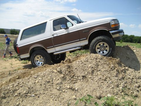 1993 Ford Bronco - This 1993 Ford Bronco features a two-tone paint scheme and aftermarket wheels, shown navigating a dirt mound.