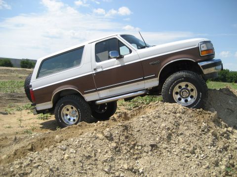 1993 Ford Bronco - This 1993 Ford Bronco is shown off-road, ascending a pile of dirt under a partly cloudy sky.