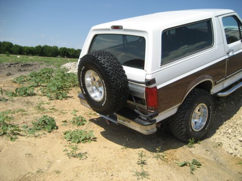 1993 Ford Bronco - Rear view of a lifted white Ford Bronco with wood paneling and a spare tire on the back.