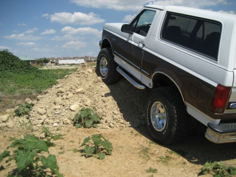 1993 Ford Bronco - This lifted 1993 Ford Bronco navigates a dirt incline under a partly cloudy sky.