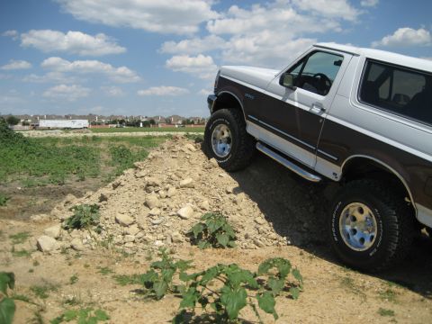 1993 Ford Bronco - Ford Bronco ascends a pile of dirt under a partly cloudy sky with houses in the background.