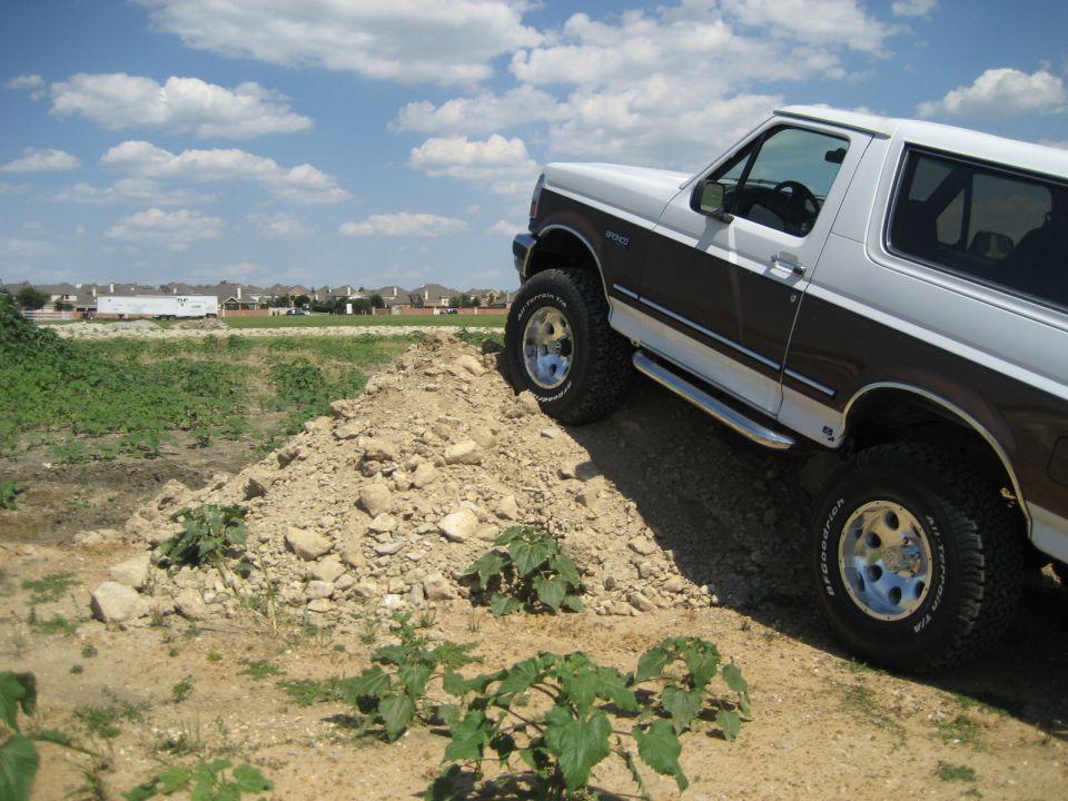 1993 Ford Bronco with lifted suspension and off-road tires climbing a dirt mound