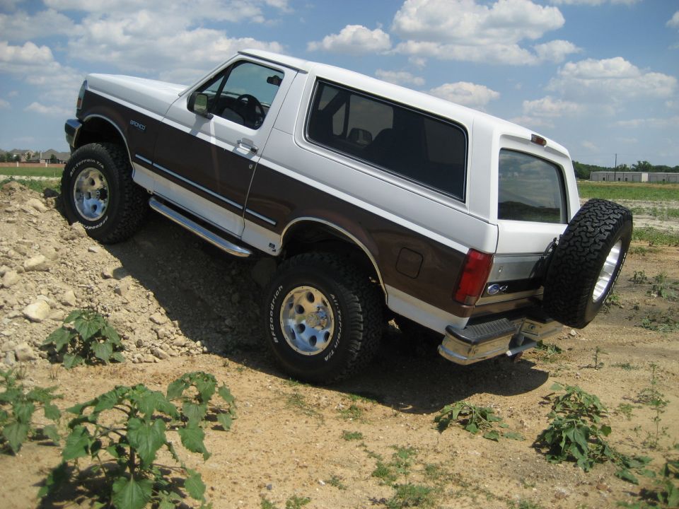 White and brown Ford Bronco on a dirt incline. It has a spare tire mounted on the back