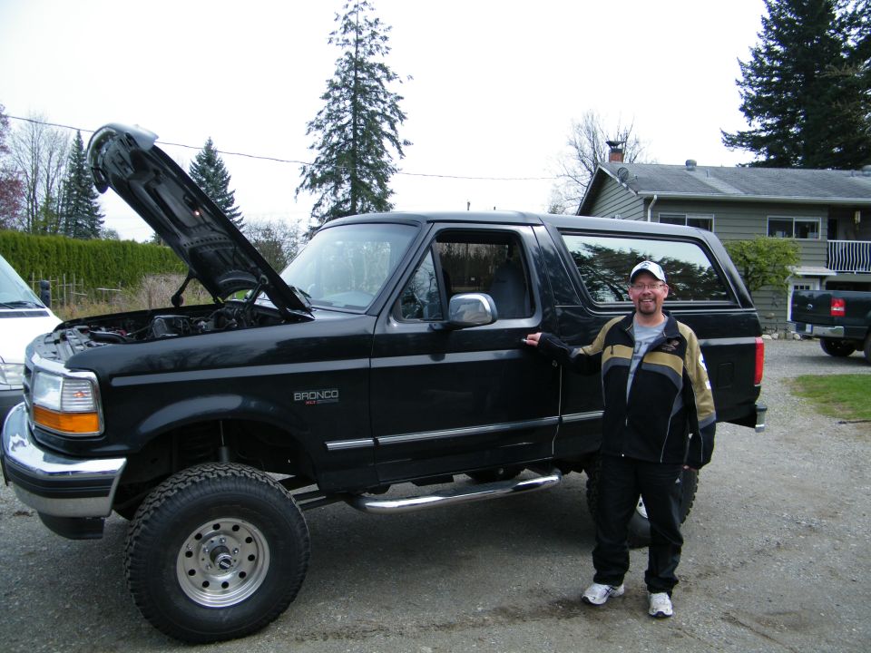 Black 1996 Ford Bronco with hood open, man standing beside driver's door