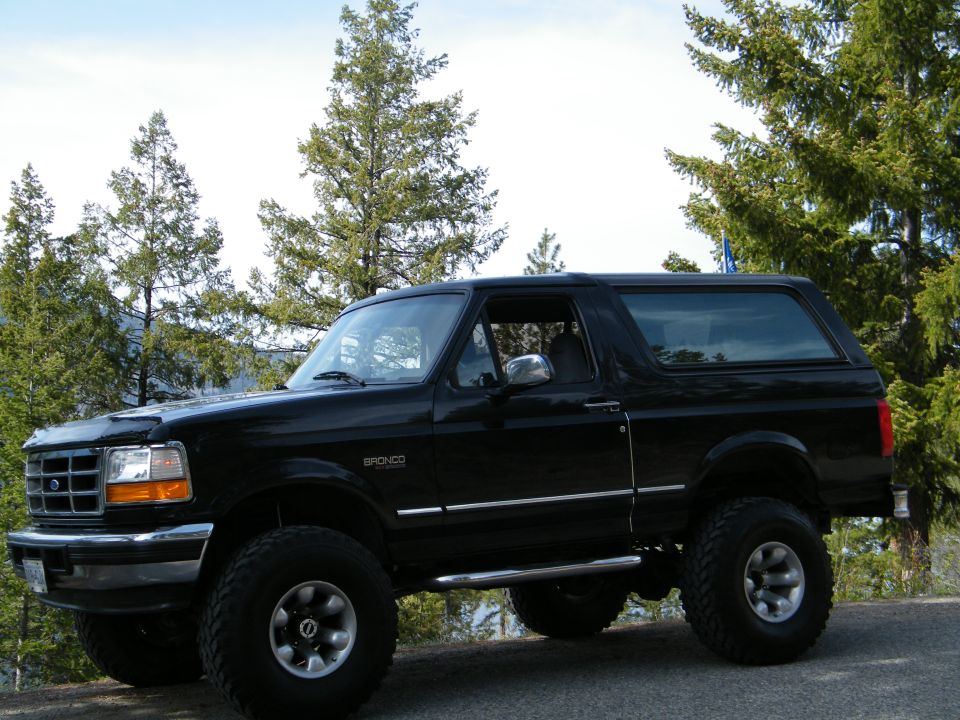 Lifted black Ford Bronco SUV on mud tires parked at a forested overlook