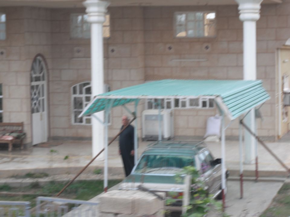 Green SUV parked under a teal carport next to a man