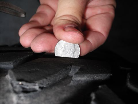 1991 Ford Bronco - A hand is using a nickel to check the tread depth of a tire.
