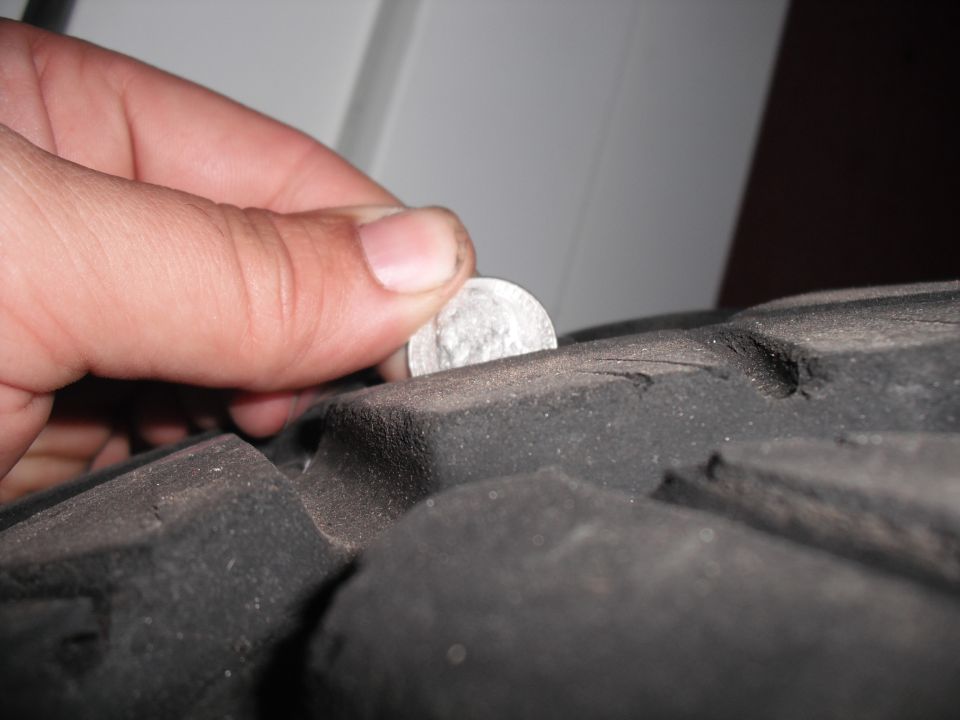 Hand holding a coin to measure tread depth on a tire