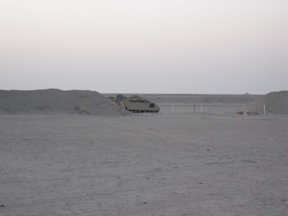 Armored personnel carrier parked in a sandy, desert area with low hills