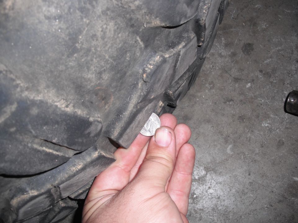 Close-up of a hand holding a quarter to measure tire tread depth on a large tire