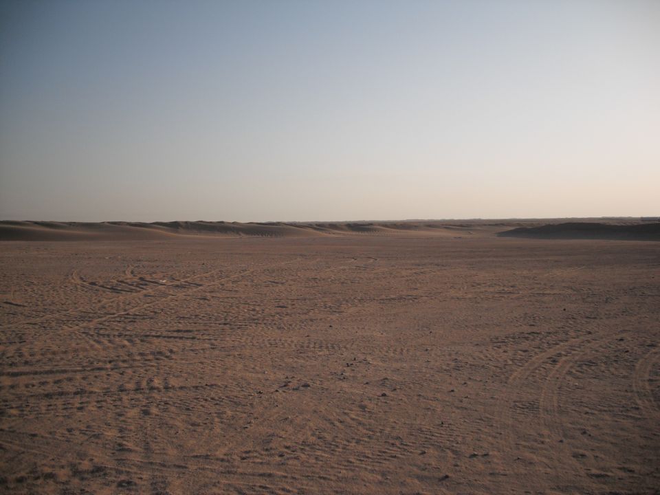 Vast desert landscape with tire tracks in the sand under a clear sky