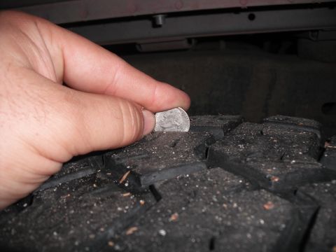 1991 Ford Bronco - A hand holds a nickel to measure the tread depth of a tire.