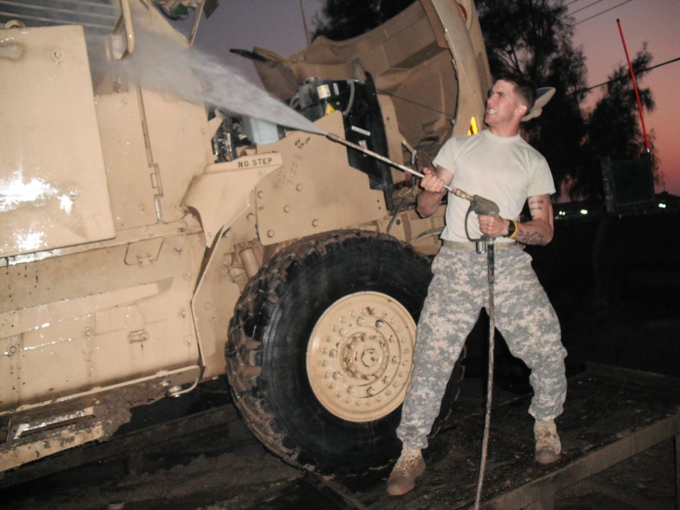 Soldier pressure washing engine compartment of tan military truck