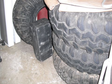 1991 Ford Bronco - Several large, aggressive tread tires are stacked together, with a black storage container nearby.