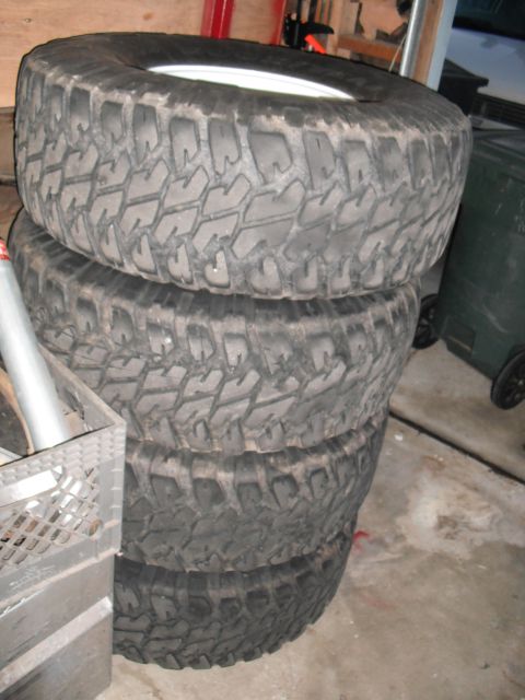 1991 Ford Bronco - Four off-road tires are stacked in a garage setting.