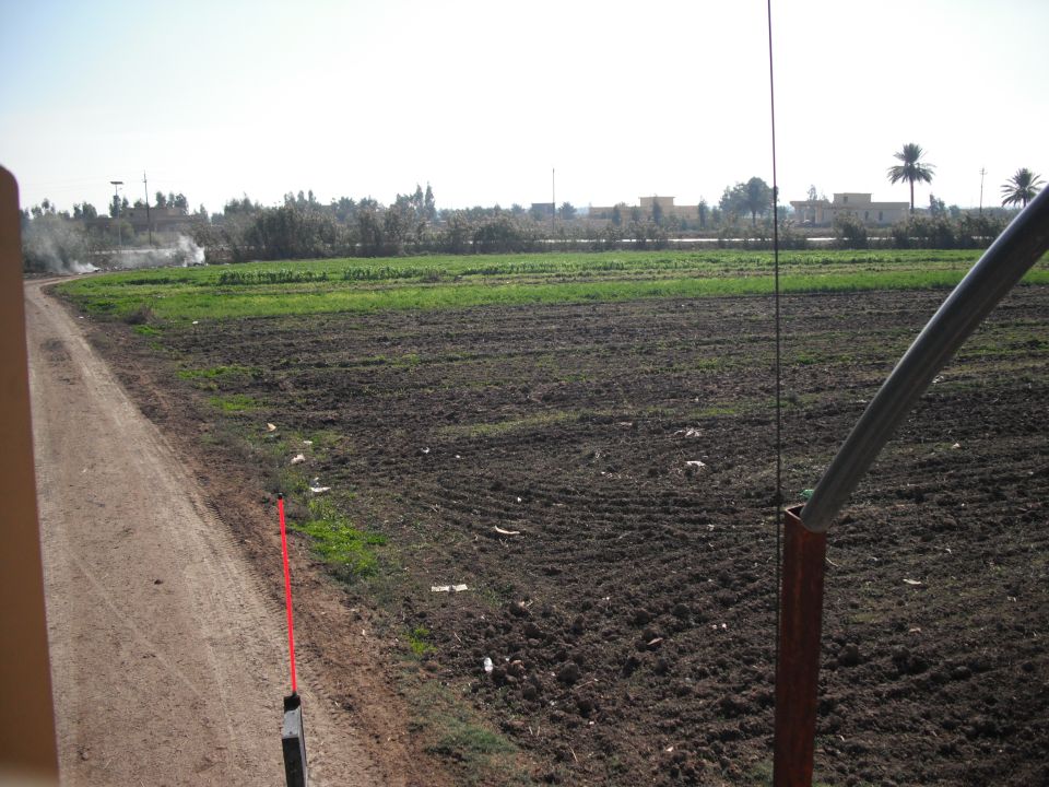 dirt road next to a field with smoke in the distance