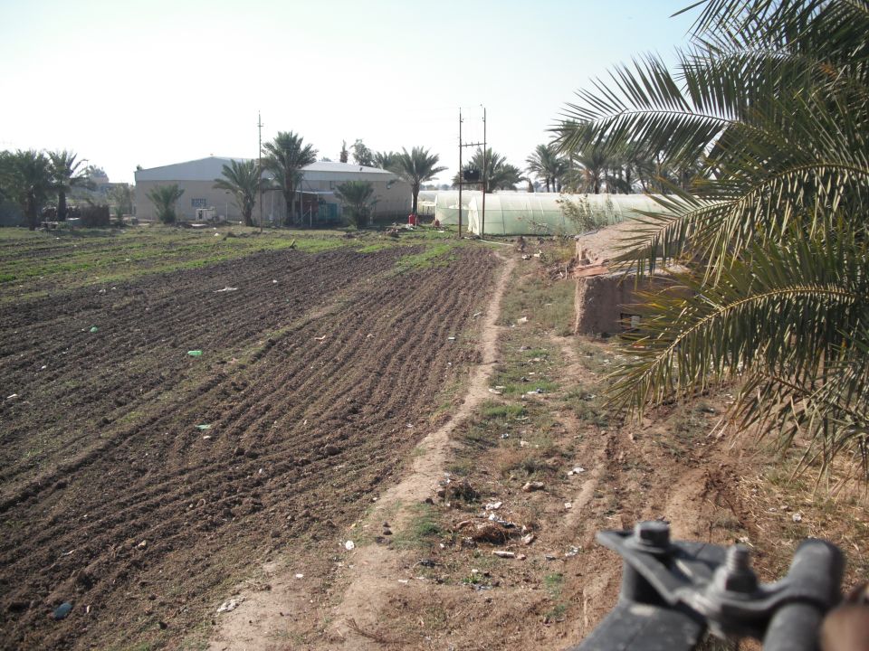 Part of a black vehicle in the foreground, with a dirt road and fields behind
