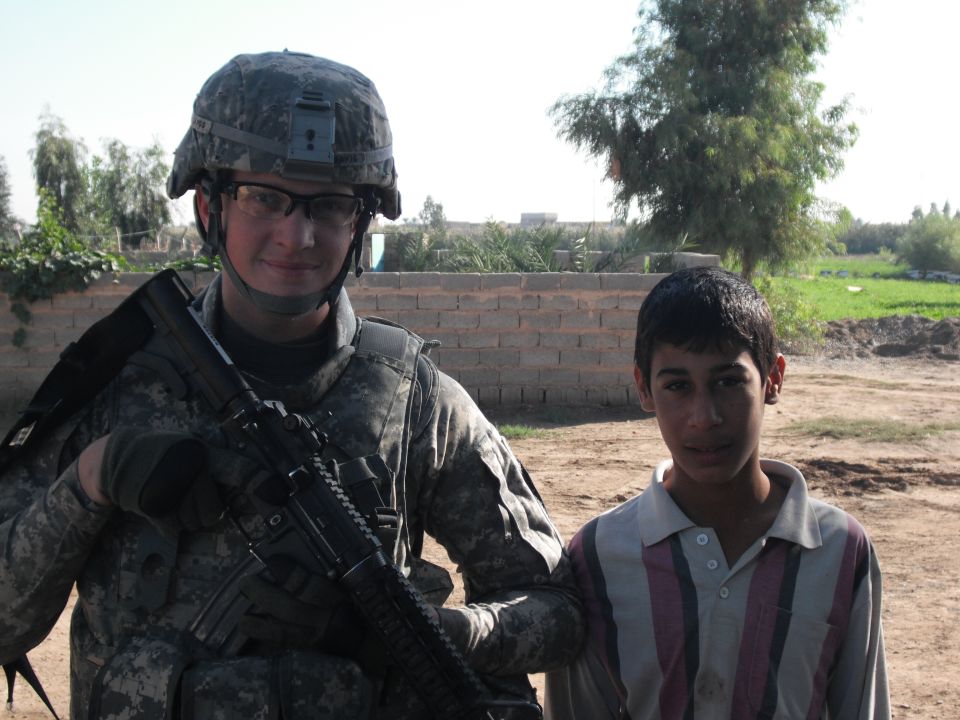 Soldier with rifle and a young boy stand in front of a brick wall