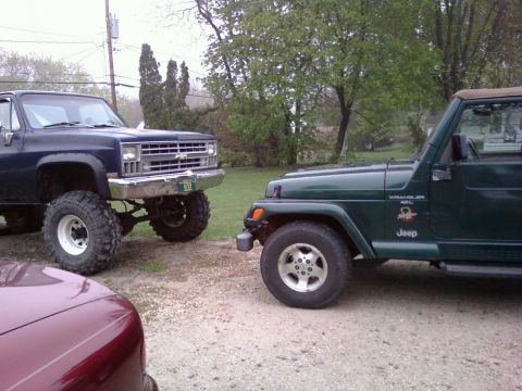 1988 Ford F-150 - A lifted pickup truck and a Jeep Wrangler are parked side-by-side on a gravel surface.