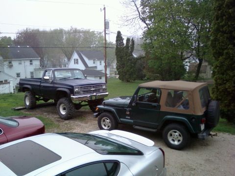 1988 Ford F-150 - A lifted, dark blue pickup truck is parked next to a green Jeep.