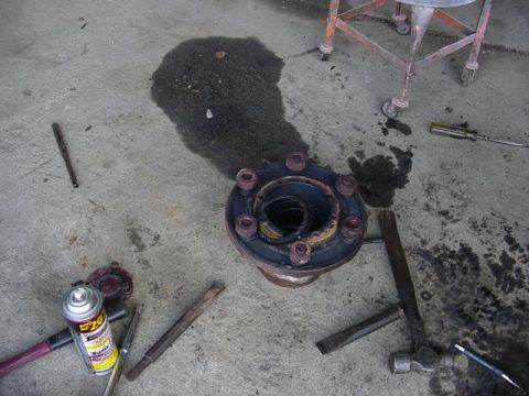 1992 Ford Bronco - A greasy eight-lug hub/knuckle assembly sits on a stained concrete garage floor mid-disassembly, its wheel studs and dark oily gear housing…
