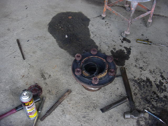 Greasy eight-lug axle hub torn down on garage floor with hammer, punches and penetrating spray